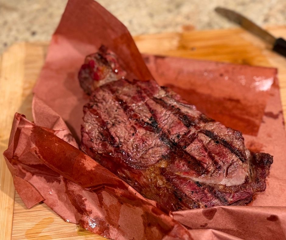 Grilled Grassfed Ribeye steak on red paper with a wooden cutting board